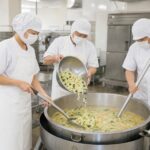 学校給食の清潔な調理場で大釜を使って調理するスタッフ